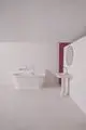 Badezimmeransicht mit einer weißen Badewanne, einem weißen Waschbecken mit Ideal Standard Armatur und einem runden Spiegel vor einer hellen Wand mit rotem Akzent.